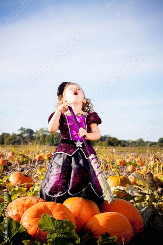 Happy Halloween! Cute cheerful little witch with a magic wand. Beautiful child girl in witch costume sitting on the big pumpkin, conjuring and laughing.