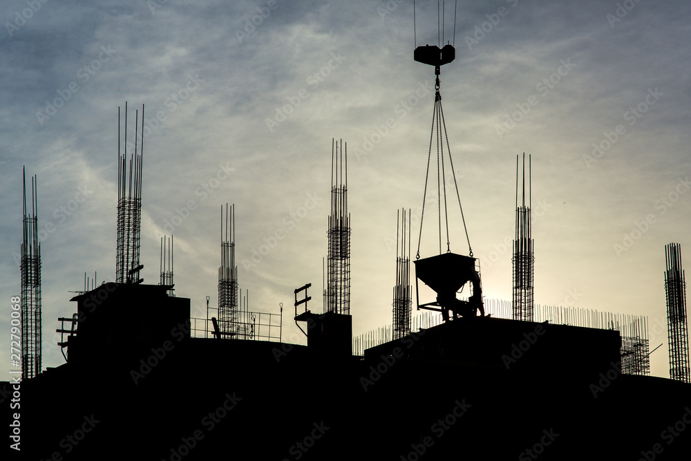 the construction of a multistory building at sunset against the sunlight of the building and workers in silhouette.