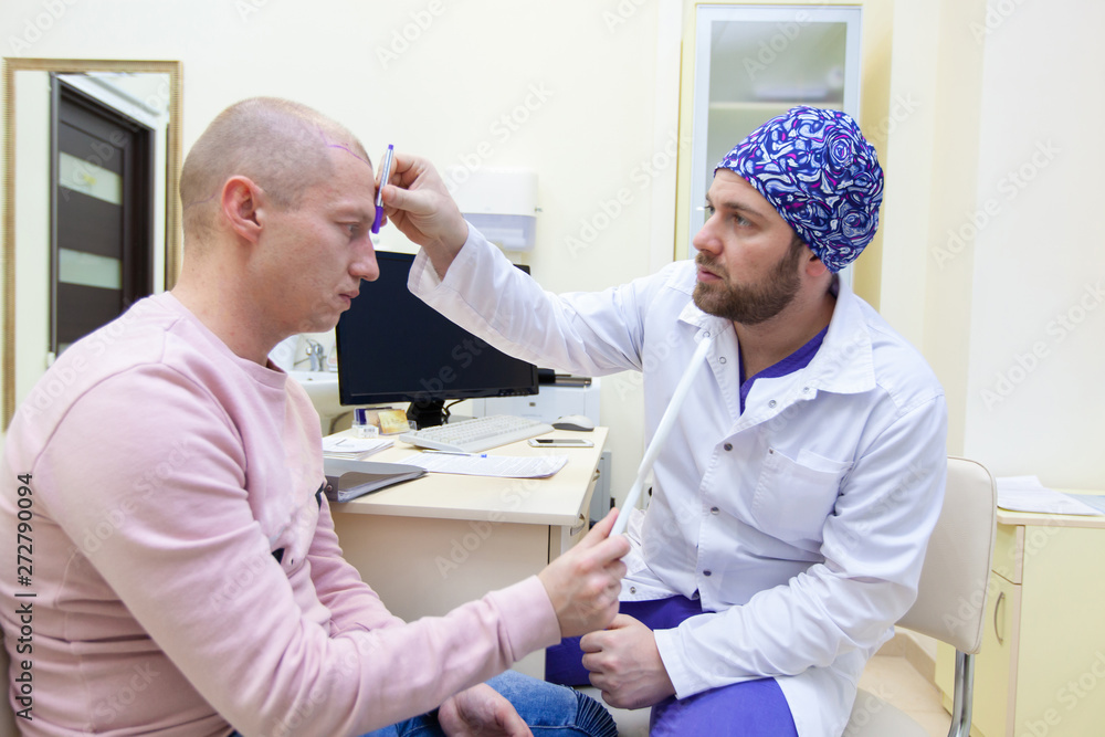 Obraz premium Baldness treatment. Patient suffering from hair loss in consultation with a doctor. Preparation for hair transplant surgery. The line marking the growth of hair. The patient controls the marking in