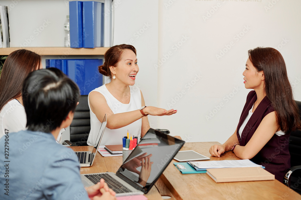 Excited female leader discussing working moments with other businesswomen while they sitting at the table in board room Excited female leader discussing working moments with other businesswomen while they sitting at the table in board room