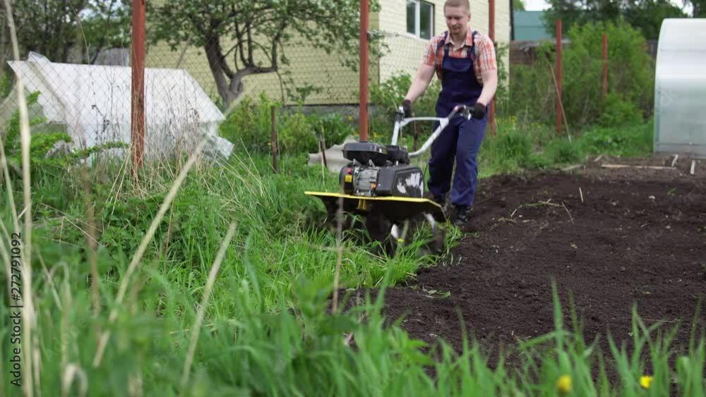 Young blond muscular farmer cultivates ground soil with rotary mini tiller before planting in springtime, technology modern farming. Young blond muscular farmer cultivates ground soil with rotary mini tiller before planting in springtime, technology modern farming.