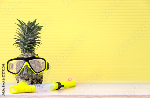 The attractive pineapples in snorkel mask with yellow background platform with copy space. Vacation and travel items. Tropical summer vacation concept. 