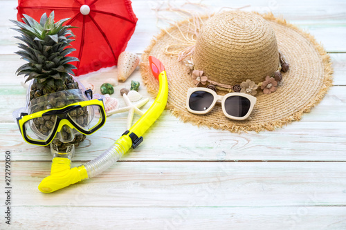 The attractive pineapples in snorkeling mask, sun glasses, red umbrella and hat on light wooden. Vacation and travel items. Tropical summer vacation concept.