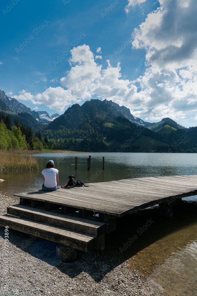 woman tourist and pet dog enjoy the summer lakeside view at the Schwarzsee Lake in the Swiss Alps in canton Fribourg