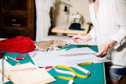 Hands of lady tailor working in her studio, tools and fabric samples on the sewing table