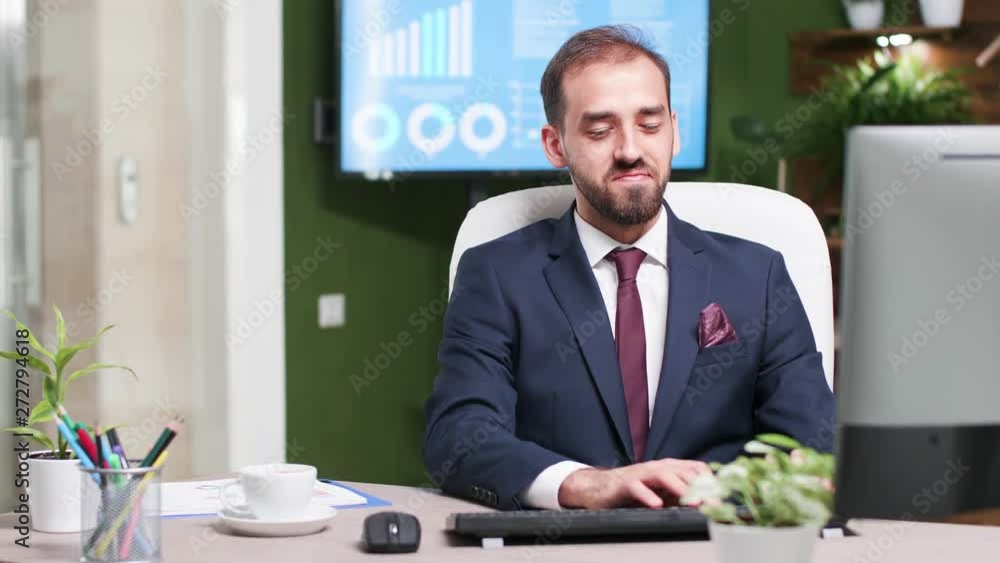 Smiling sales person in business suit working on computer in modern office with creative design. TV in the background displays sales statistics Smiling sales person in business suit working on computer in modern office with creative design. TV in the background displays sales statistics