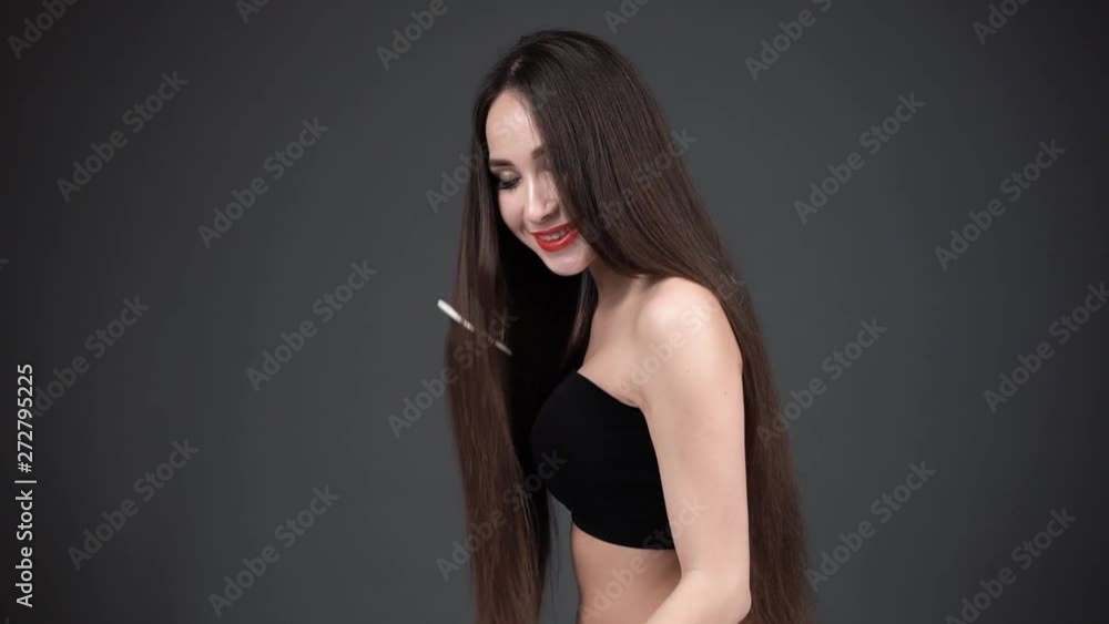 young woman combing hair with comb. Woman with luxurious hair is smiling. Dark background young woman combing hair with comb. Woman with luxurious hair is smiling. Dark background