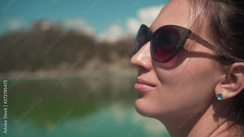 A young woman in sunglasses sits by the lake on a spring day, relaxing in nature. Close-up girl. Rest, harmony with nature. A young woman in sunglasses sits by the lake on a spring day, relaxing in nature. Close-up girl. Rest, harmony with nature.