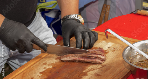 Chef cuts grilled beef and prepares rump steak with chimichurri sauce for visitors photo