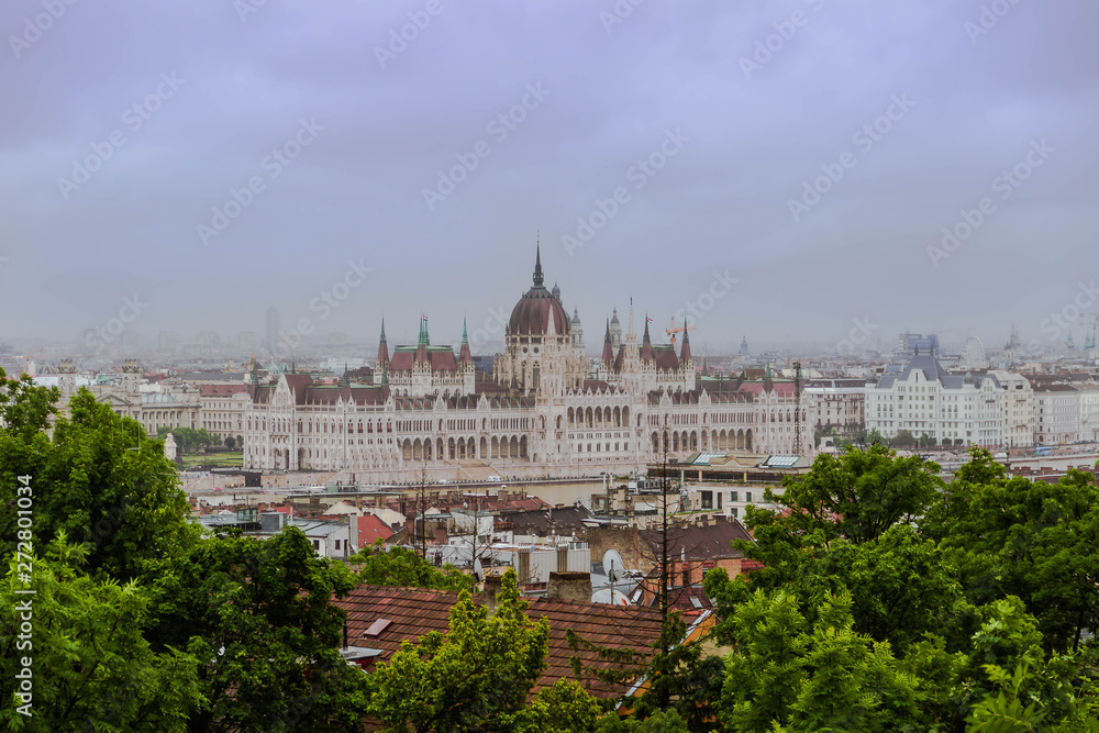 Parliament building over the red roofs of the old houses in Budapest on a cloudy rainy foggy day.