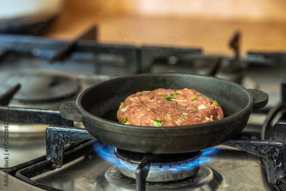 Iron pan with raw cutlet on a gas stove.