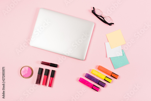 top view of laptop, glasses, highlighters and decorative cosmetics on pink