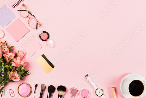 top view of cup of coffee, flowers, decorative cosmetics and credit card on pink