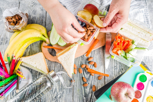 Billede på lærred Mother cooking school lunch box set, Preparing healthy snacks - cheese sandwich with cucumber, carrot