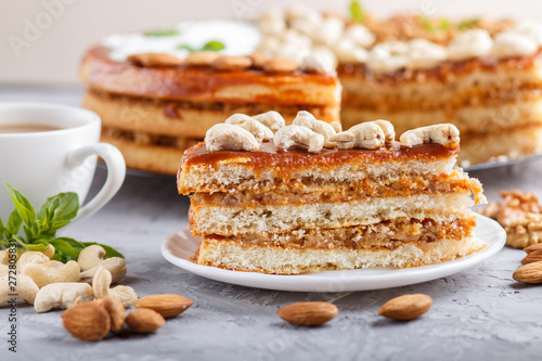 Piece of homemade cake with caramel cream and nuts with cup of coffee on a gray concrete background, side view.