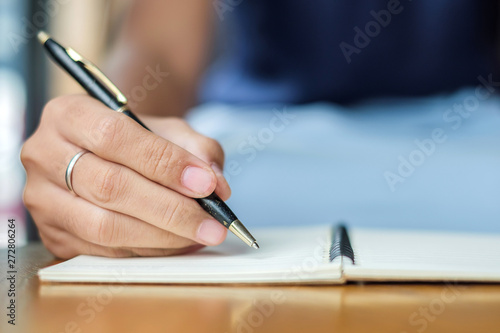 Businesswoman writing something on notebook in office, hand of woman holding pen with signature on paper report. business concepts