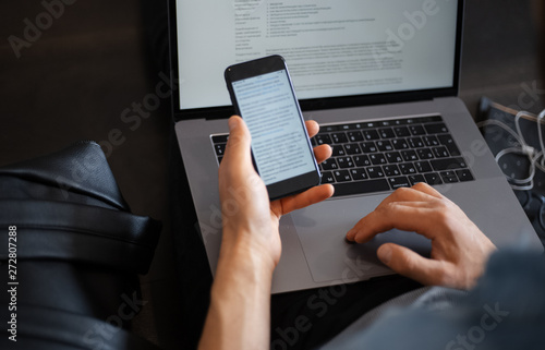 man working at the laptop sitting on the floor with smartphone and coffee in his hands