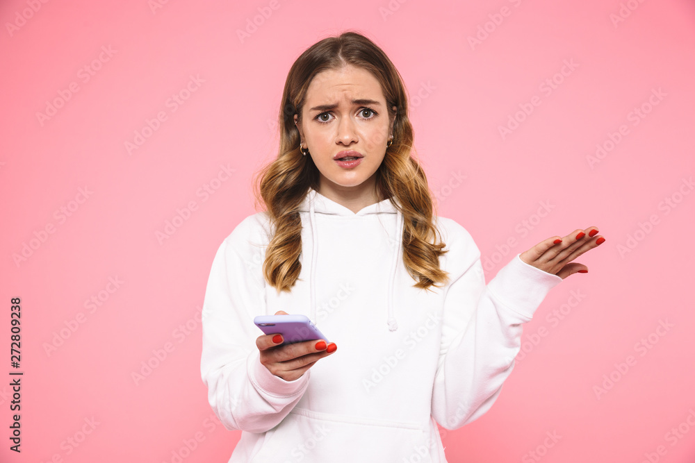 Displeased blonde woman wearing in casual clothes holding smartphone Displeased blonde woman wearing in casual clothes holding smartphone