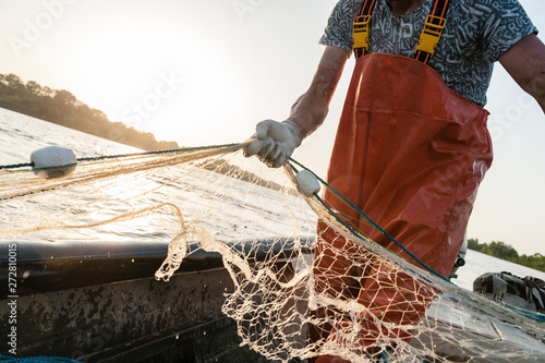 Fotografia Dynamic composition with a fisherman dressed in an orange rompers gathering his trammel net during a fishing trip on the Danube river