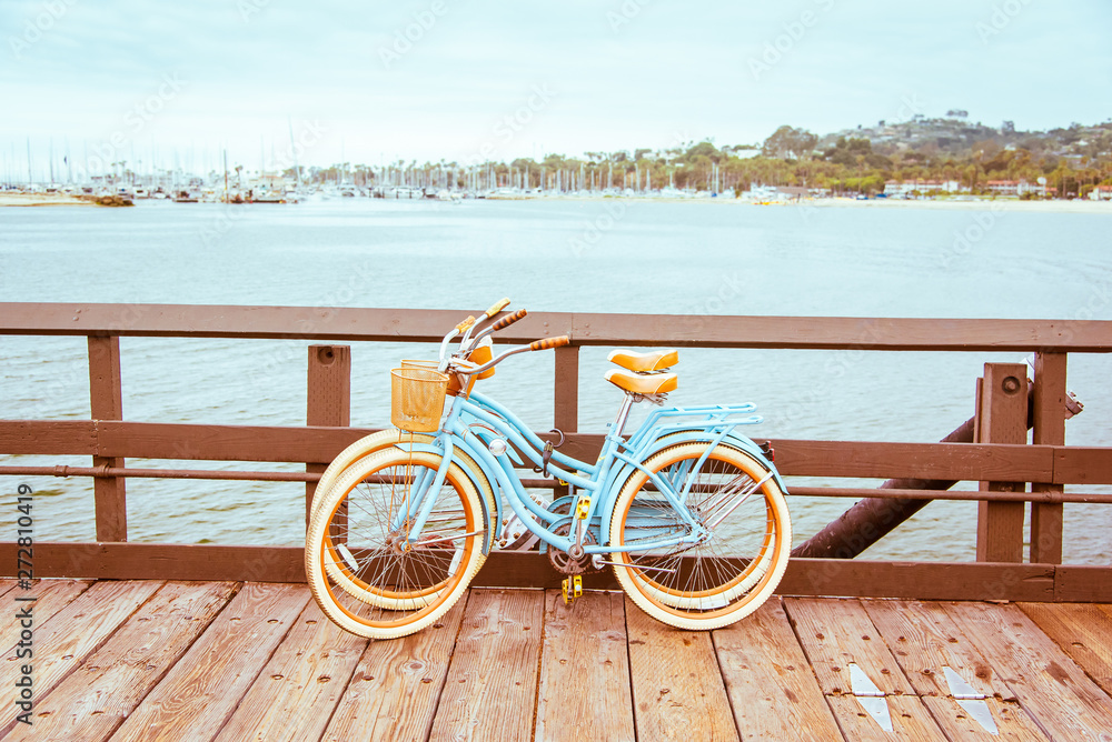 Santa Barbara romantic concept on sea, beach, yacht club panorama background. Two retro bicycles standing on Santa Barbara pier, California, USA. Vintage filter with muted teal blue and orange colors. - obrazy, fototapety, plakaty 