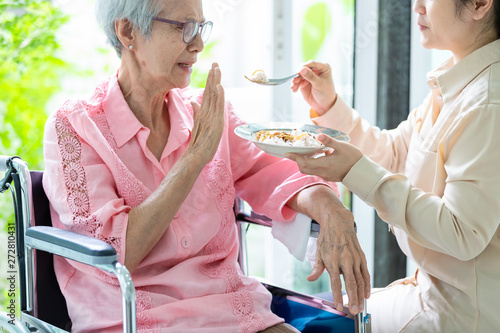 Unhappy asian senior woman rejecting,gesture hand “NO” elderly patient bored with food or boredom,old people getting sick and tired of food in wheelchair at home,loss of appetite,anorexia concept