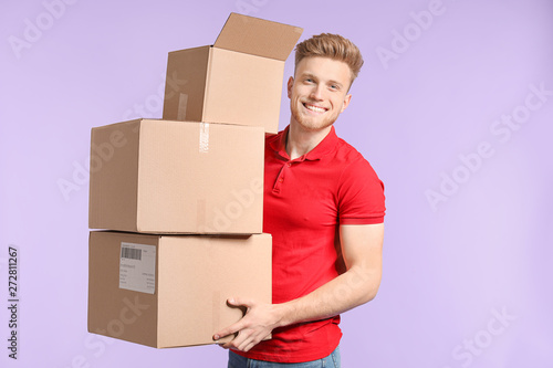 Young man with cardboard boxes on color background