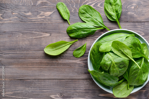 Plate with fresh spinach on wooden table