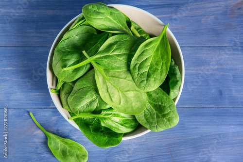 Bowl with fresh spinach on color wooden background