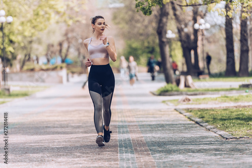 attractive sportswoman jogging along wide alley in green park