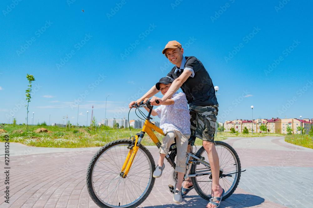 Fototapeta premium Older and younger brothers ride a bike