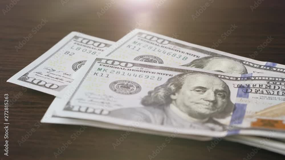 One hundred dollar bills fall on a wooden surface One hundred dollar bills fall on a wooden surface