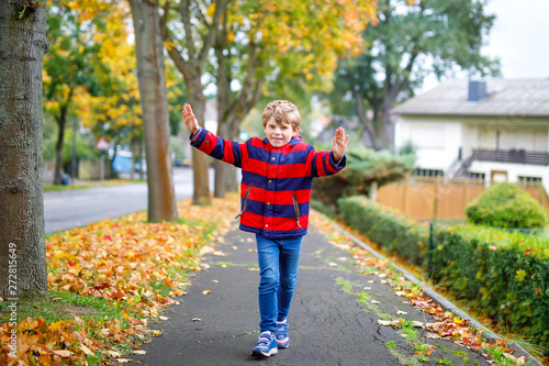 Happy little boy running on autumnal street after school. Kid happy about school vacations. Child with autumn fashion clothes walking in the city.