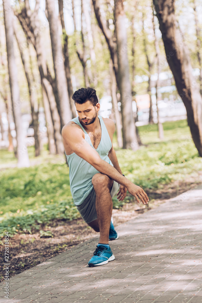 handsome man in sportswear working out and stretching in green park