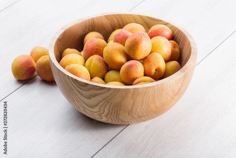ripe organic apricots fruits in ash tree wooden bowl on a white wooden background ripe organic apricots fruits in ash tree wooden bowl on a white wooden background