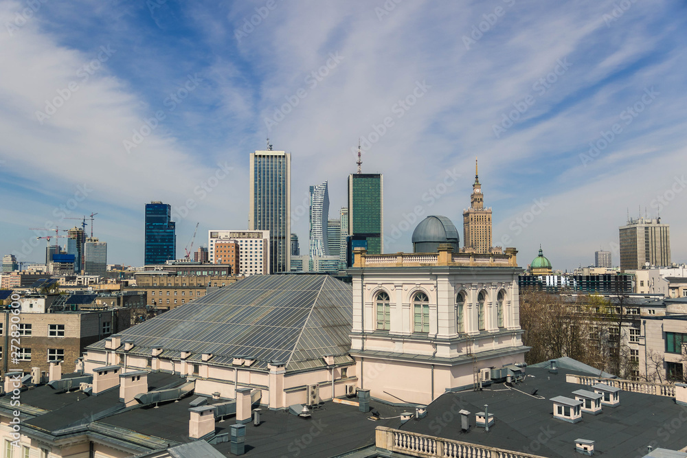 Warsaw unusual cityscape with modern skyscapers and historic buildings and roofs inder the blue cloudy sky.