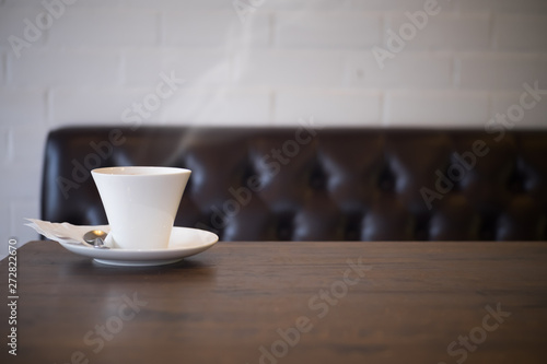 White cup of coffee on wooden table in the cafe, free space with old brown vintage sofa background.