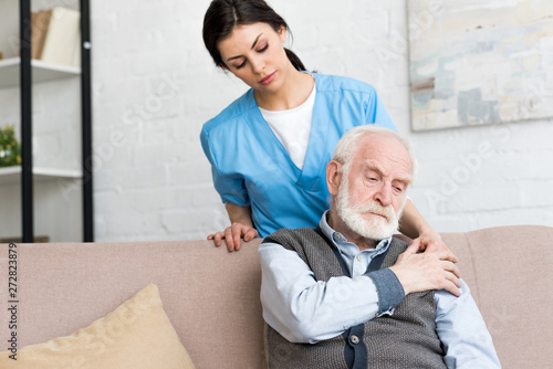 Doctor standing behind sad senior man, putting hand on his shoulder