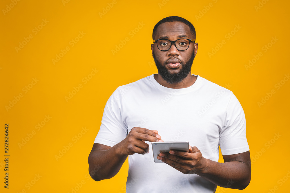 Working on digital tablet. Rear view of young African american man working on digital tablet while standing isolated on yellow background. Working on digital tablet. Rear view of young African american man working on digital tablet while standing isolated on yellow background.