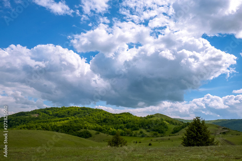 Green field and beautiful sunny day. In the sky are thick white robes and blue sky among them. View of the nearby hill in front. © Slobodan Radovanovic