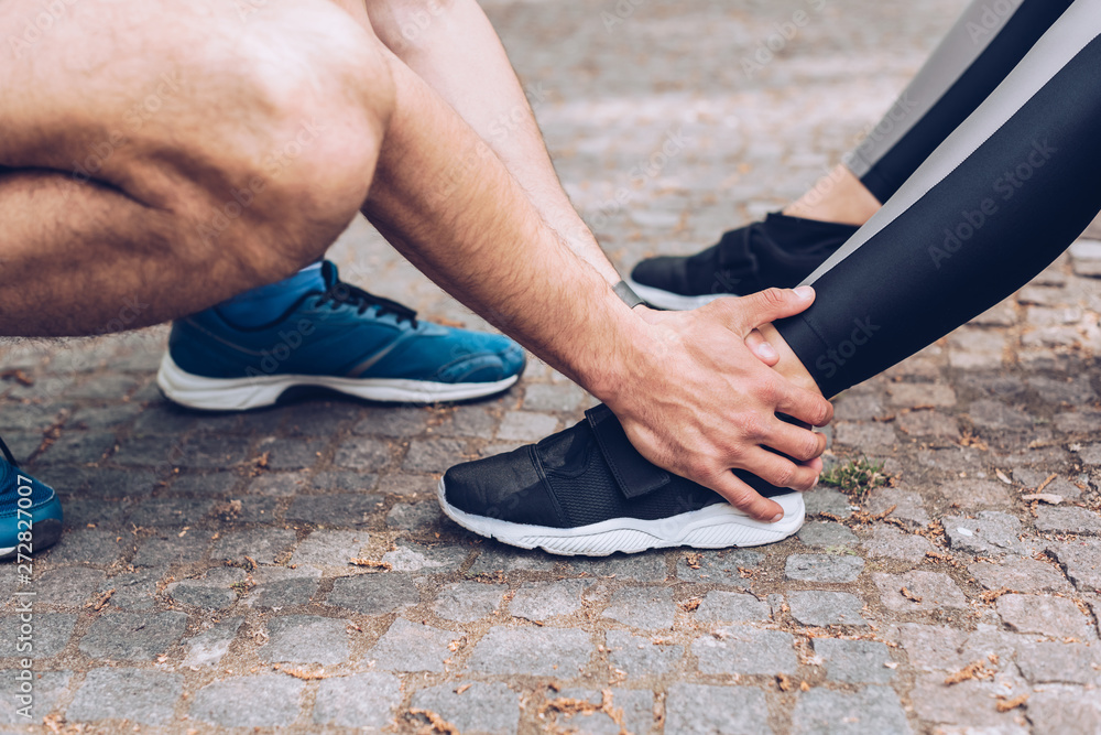 cropped shot of sportsman touching injured leg of sportswoman in sneakers