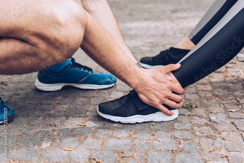 cropped shot of sportsman touching injured leg of sportswoman in sneakers