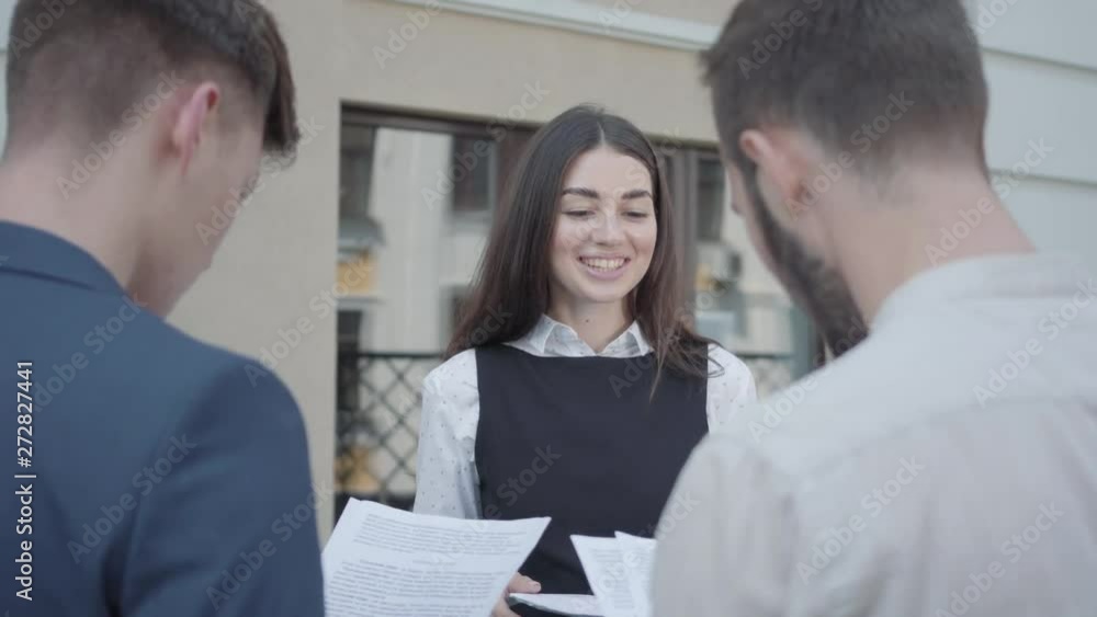 Young woman and two men in formal wear discussing documents on the terrace. The girl giving papers to colleagues. Business relationship. Concept of freelance, distant work. The guys working outdoors Young woman and two men in formal wear discussing documents on the terrace. The girl giving papers to colleagues. Business relationship. Concept of freelance, distant work. The guys working outdoors