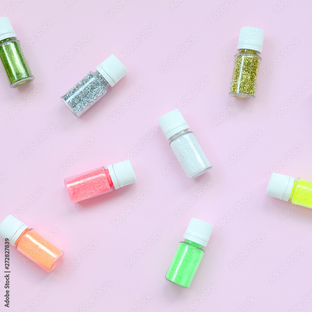 A flat lay pattern with colorful glitter bottles lies on pastel pink background. Many round jars with multi-colored bright sparkles for nail polish. Sparkling sequins. Top view A flat lay pattern with colorful glitter bottles lies on pastel pink background. Many round jars with multi-colored bright sparkles for nail polish. Sparkling sequins. Top view