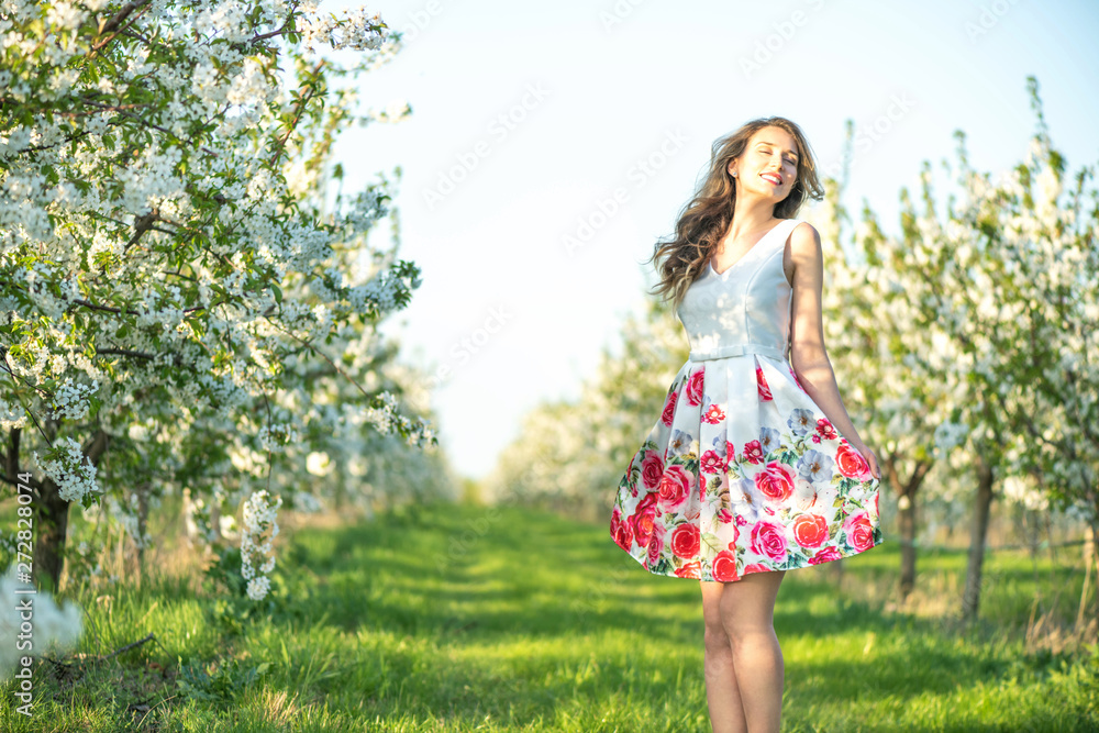 Happy Woman in an orchard at springtime. Enjoying sunny warm day. Retro style dress. Blooming blossom cherry trees. Colorful spring moods Happy Woman in an orchard at springtime. Enjoying sunny warm day. Retro style dress. Blooming blossom cherry trees. Colorful spring moods
