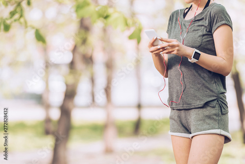 cropped shot of sportswoman in fitness tracker using smartphone and listening music in earphones