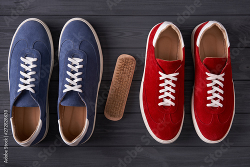 Top view of red and blue casual unisex suede sneakers with cleaning brush