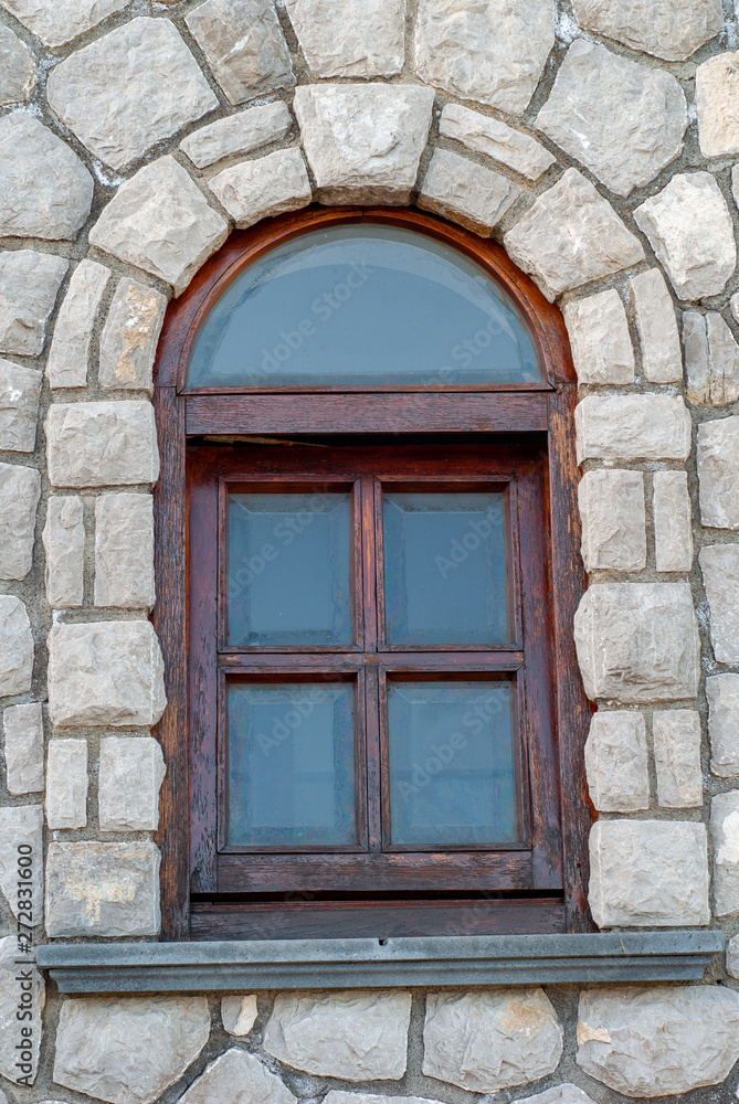 Arched wooden window, on a stone wall, with rusticated glass