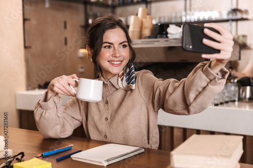 Beautiful woman take a selfie by mobile phone indoors in cafe.