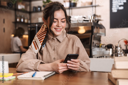Happy young beautiful woman using mobile phone indoors in cafe.