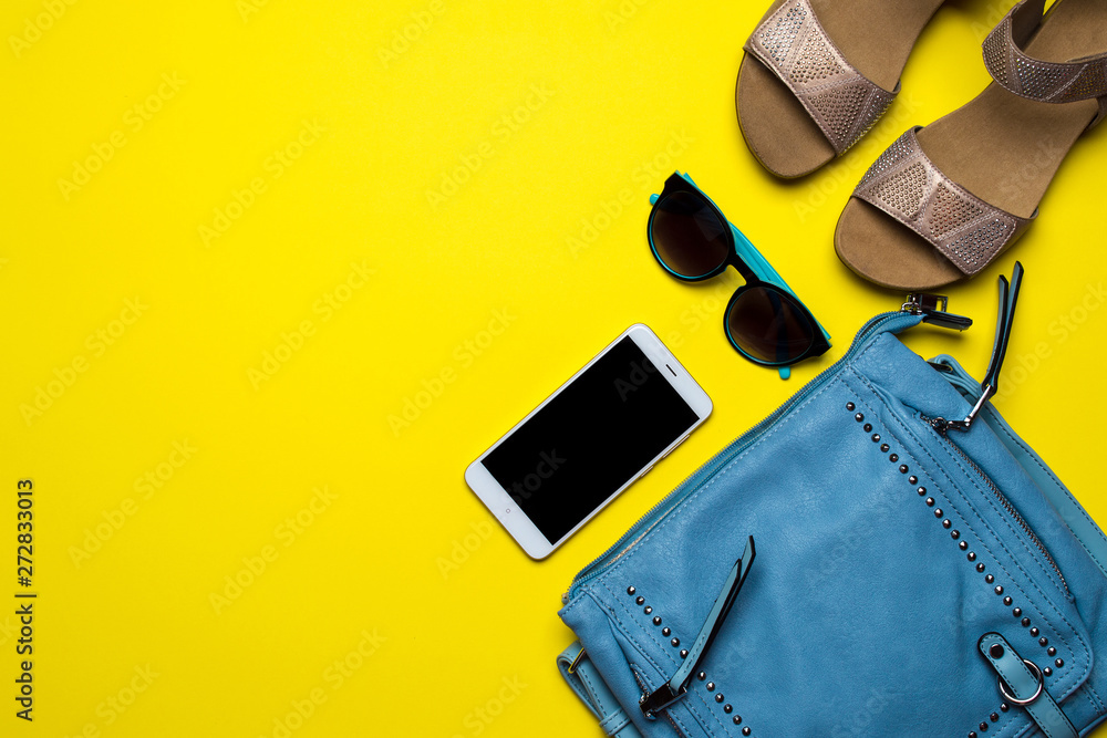 Ladies handbag stuff flat lay yellow background. Overhead view of women's handbag, sandals, smartphone and glasses.